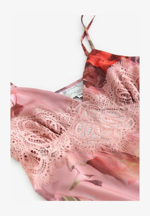 Lyserød blomstrede satin camisole med indviklet blonderdetalje langs brystet og tynde skulderstropper på hvid baggrund.