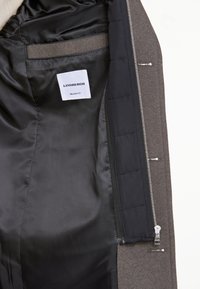 Giacca grigia con interno in satin nero, con etichetta "LINDBERGH" e "FIT CONFORTEVOLE". Include una tasca con zip e una texture liscia.