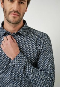 Langarmhemd mit blauem Musterdesign, klassischem Kragen und strukturiertem Stoff mit subtilem Glanz.