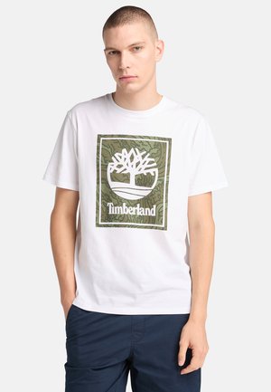 Witte katoenen T-shirt met een groen camouflage boomlogo in een rechthoekig ontwerp met daaronder de tekst "Timberland". Korte mouwen en ronde hals.