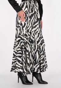 Gestufter Maxi-Rock mit schwarz-weißen Zebra-Streifen und Rüsche am Saum, aus leichtem Stoff, kombiniert mit schwarzen spitzen High Heels.