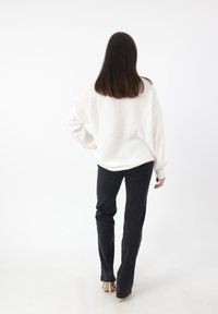Oversized witte gebreide sweater met geribbelde manchetten, gecombineerd met strakke zwarte jeans en beige hoge hakken. Gladde, zachte textuur.