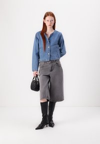 Τζάκετ τζιν σε ανοιχτό μπλε χρώμα με μπροστινά κουμπιά, συνδυασμένο με γκρίζες φαρδιές σορτς, μαύρες μπότες μέχρι το γόνατο και μια μικρή υφασμάτινη μαύρη τσάντα.