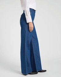 Saias de ganga azuis de perna larga com costuras visíveis e uma cintura alta. Estilizadas com uma camisa branca de colarinho e calçado preto.