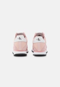 Zapatillas rosas con parte superior de gamuza y malla, detalles en blanco en el talón y suela de goma negra. Cuenta con un logo en la parte trasera del talón.