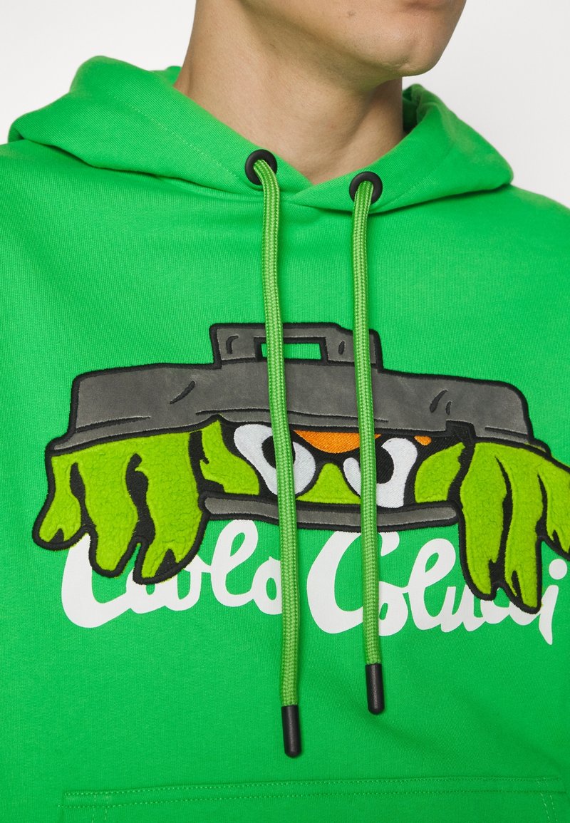 Sweat à capuche vert vif avec cordons montrant une poubelle dessin animé avec des mains et des yeux verts qui dépassent au-dessus d'un texte blanc en cursive.