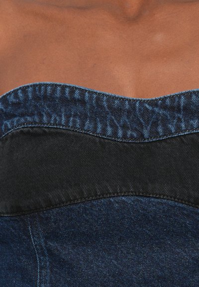 Denim corset with a structured black panel at the top. Features dark wash, soft texture, curved neckline, and contrasting stitching detail.