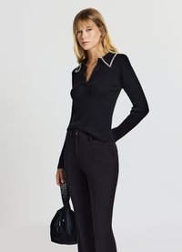 Maglione nero a coste con scollo a V, impreziosito da dettagli di perle sul colletto, abbinato a pantaloni neri su misura e una borsa strutturata.