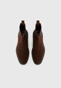 Botas de tobillo de ante marrón con un acabado suave, paneles laterales elásticos y suela de goma negra. Tiras de acceso para ponerlas fácilmente.
