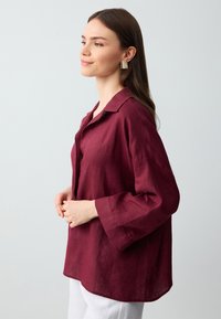 Burgundowa lniana koszula z kołnierzykiem, długimi rękawami i lekko luźnym krojem. Posiada czysty dół i subtelną fakturę.