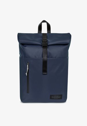 Sac à dos à rabat roulé de couleur marine en tissu imperméable. Comprend une poche zippée à l'avant et une sangle à boucle noire. Équipé d'une poignée de transport.