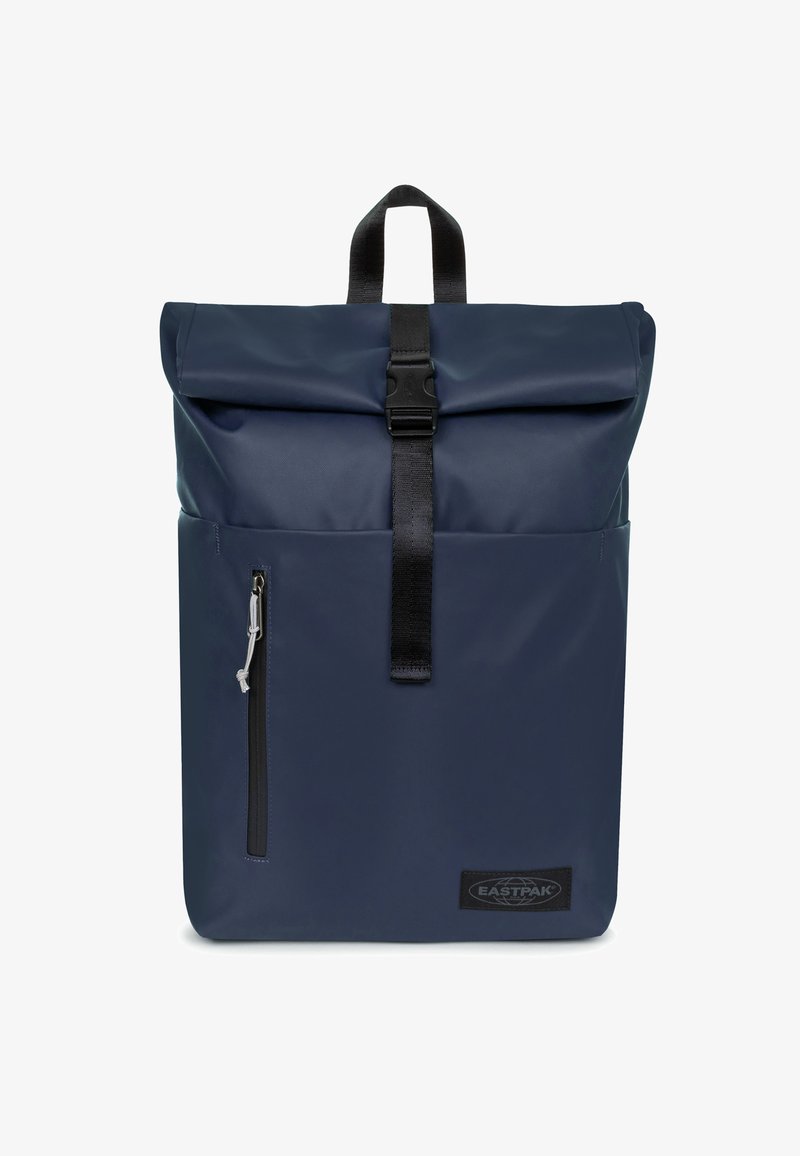 Sac à dos à rabat roulé de couleur marine en tissu imperméable. Comprend une poche zippée à l'avant et une sangle à boucle noire. Équipé d'une poignée de transport.