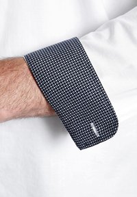 Marinefarbener Umschlag mit einem geometrischen Muster aus kleinen weißen Kreisen. Baumwollstoff mit einer klaren, glatten Textur. Weißes Hemd darunter.