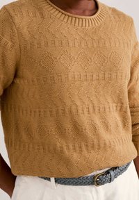 Sweter w musztardowym kolorze, dzianinowy, z geometrycznymi wzorami i ściągaczem przy dekolcie, zestawiony z szarym plecionym paskiem z metalową klamrą.