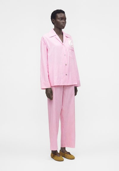 Γυναίκα φοράει μακριμάνικο πουκάμισο με ροζ και λευκές ρίγες και παντελόνι με φαρδύ πόδι στο ίδιο σχέδιο, σε συνδυασμό με καφέ πλεκτά παπούτσια με επίπεδη σόλα.