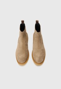 Bottines Chelsea en daim tan avec panneaux latéraux en élastique, bout arrondi et semelle en caoutchouc beige contrastante. Aucune marque ni motif visible.