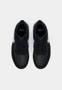 Svarte og hvite høye sneakers med svarte snøringer, perforerte tåhetter og merkede såler, vist ovenfra på en ensfarget bakgrunn.