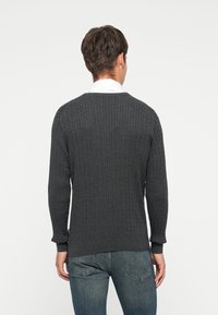 Mørk grå ribbestrikket genser med lange ermer og rund hals, kombinert med blå jeans. Strukturert stoff med en figurnær silhuett.