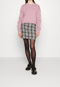 Rosa sweatshirt med vita randiga ärmar, tillsammans med en svart och vit rutig mini-skjorta. Genomskinliga svarta strumpbyxor och svarta spänneskor fulländar looken.