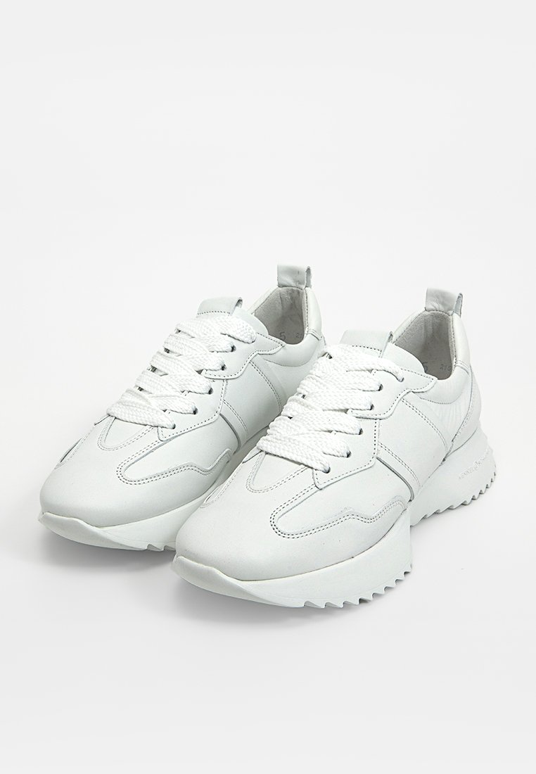 Weiße Sportschuhe mit einem glatten Lederoberteil, strukturierten Details, runder Zehenpartie, Schnürverschluss und einer dickeren Gummisohle mit Rillen.