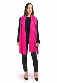 Lys pink tørklæde lavet af blødt materiale, der elegant hænger om halsen, parret med en sort top og tætsiddende bukser, iført højhælede sko.