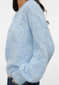 Gaiši zils adīts džemperis ar ziedu izšuvumiem, ribotām aprocēm un mīkstu tekstūru, ar vaļēju piegriezumu.