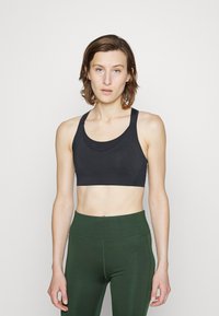 Sutien desportivo preto feito de um material suave, com decote redondo e alças largas, combinado com leggings de cintura alta em verde escuro.