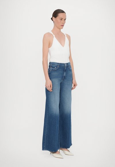White sleeveless top with a deep V-neck, paired with high-waisted blue wide-leg jeans, featuring a faded wash and subtle distressing.