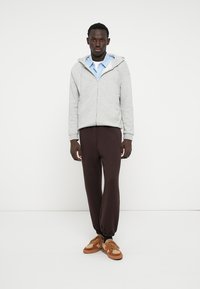 Grauer Zip-Hoodie, hellblaues Poloshirt, braune Jogginghose und beigen Sneaker. Lässiges Outfit mit lockerer Passform und Kordelzugsdetail.