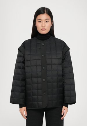 Padded black jacket with quilted texture, oversized shape, round neckline, and front button closure. Worn over a black turtleneck.