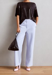 Černý top s krátkými rukávy zdobený flitry, doplněný světle modrými širokými kalhotami. Celý outfit doplňuje černá trojúhelníková kabelka a růžové boty na blokovém podpatku.