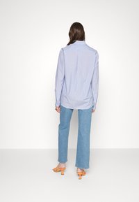 Camisa azul clara às riscas, com botões e mangas longas, de corte descontraído e aberturas laterais, combinada com calças de ganga azul clara e sapatos de salto altos laranja.