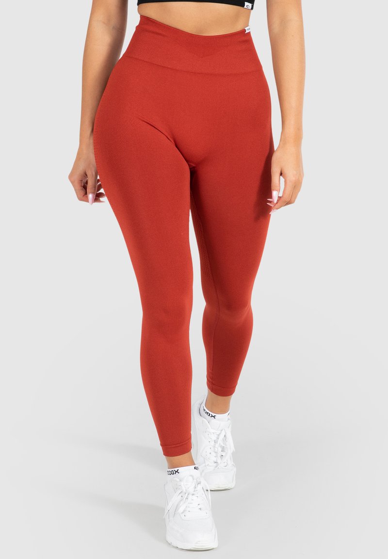 Leggings rossi a vita alta realizzati in tessuto elasticizzato con una consistenza liscia, abbinati a scarpe da ginnastica bianche.