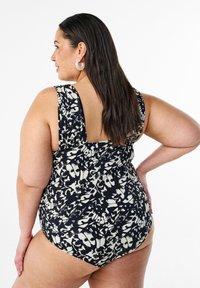 Costume da bagno a pois bianco e nero con spalline larghe, design con scollo a giro e forma aderente. Tessuto morbido con una stampa grafica astratta.