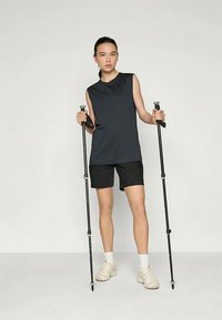 Black sleeveless top and shorts layout, holding trekking poles. Footwear is light, textured fabric. Simple design with no patterns.