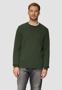 Grüner Rundhalsausschnitt-Pullover mit strukturiertem Strickmuster. Gerippte Bündchen und Saum. Subtiles Logodetail auf der linken Brust. Getragen mit grauen Jeans.