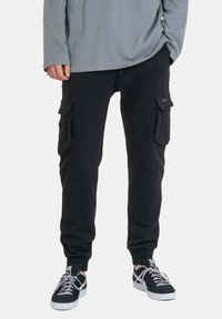 Black cargo pants featuring side pockets, a relaxed fit, cuffed ankles, and a soft cotton material, paired with black sneakers.