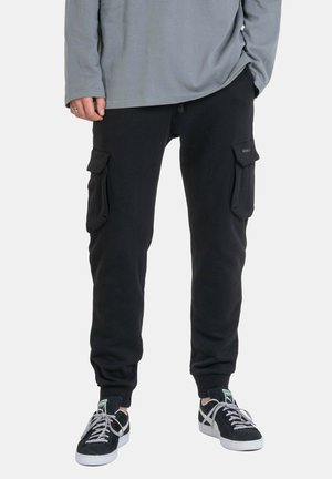Black cargo pants featuring side pockets, a relaxed fit, cuffed ankles, and a soft cotton material, paired with black sneakers.