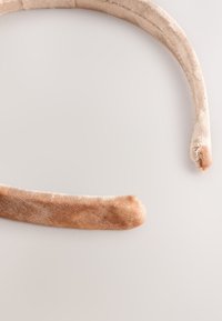 Velvet hairband in light beige, featuring a rounded design with smooth texture and slight sheen, tapering at the ends.