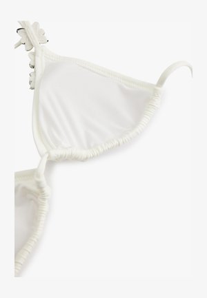 Haut de bikini blanc avec bords froncés et petites décorations en forme de fleurs le long de la couture supérieure sur fond uni.