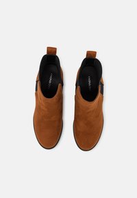 Bottines en daim marron avec des panneaux élastiques sur les côtés, des tirants et des semelles plates en caoutchouc. Texture lisse avec un design épuré et minimaliste.