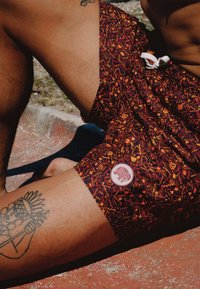 Bañadores con un patrón rojo y naranja, con un cordón blanco. Presentan un parche redondo con un diseño de animal en el lado izquierdo.