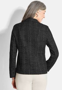 Veste noire texturée avec un motif linéaire blanc, coupe ajustée, manches longues et col cranté, présentée de dos.