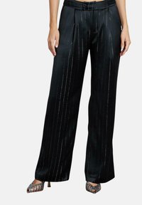 Zwarte satijnen wijde broek met zilveren streepjes, voorzien van plooien en een tailleband. Gekleed met metallic sandalen met banden.