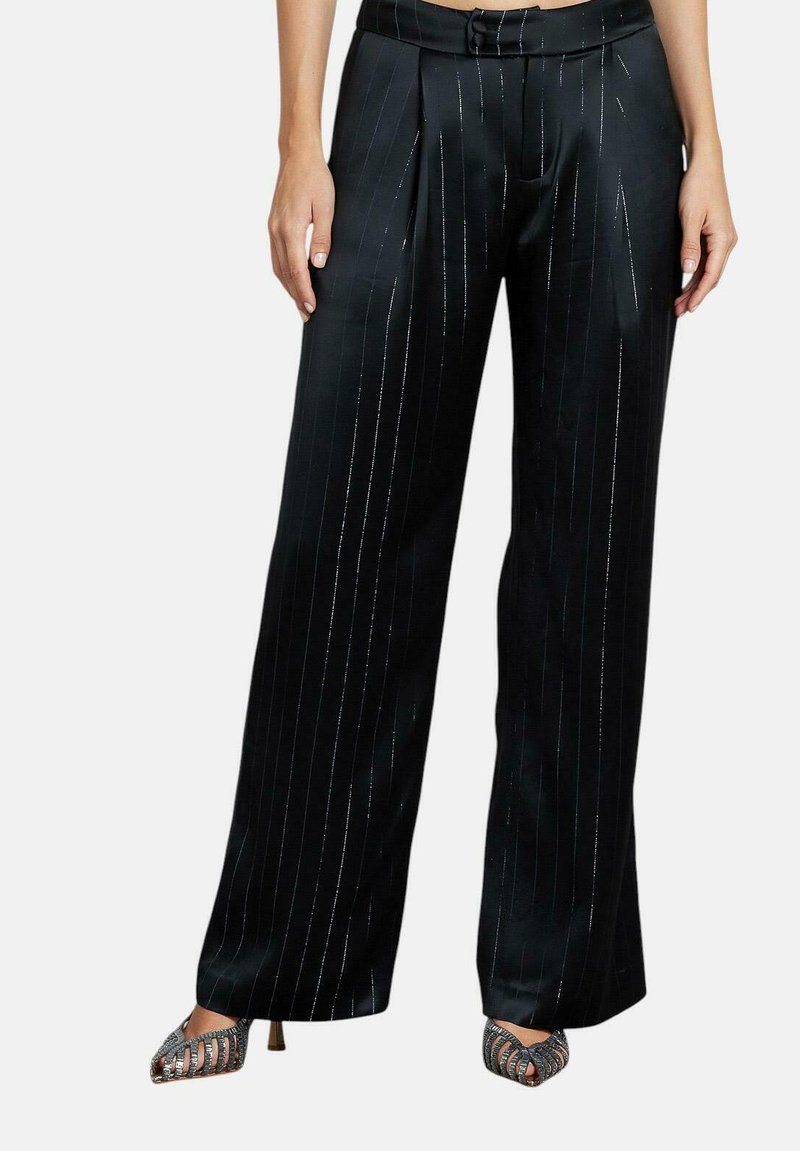 Zwarte satijnen wijde broek met zilveren streepjes, voorzien van plooien en een tailleband. Gekleed met metallic sandalen met banden.