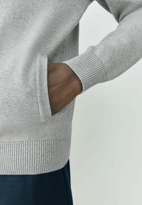 Gray knitted sweater with ribbed hem and cuffs, featuring a side pocket. Smooth texture, casual design.
