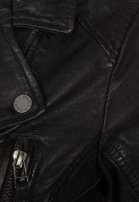 Giubbotto di pelle nera con risvolto classico, tasca con zip diagonale e bottone a pressione con marchio. La texture appare liscia con una leggera lucentezza.