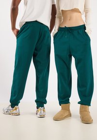 Teal sweatpants made of soft fabric with a drawstring waist, featuring side pockets and a back pocket. Worn with contrasting footwear.