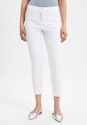 Weiße Stretch-Cotton-Hosen mit schmalem Schnitt, mittelhohem Bund, Vordertaschen und umgeschlagenen Säumen. Kombiniert mit silbernen spitzen Ballerinas.