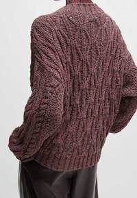 Pull en tricot épais bourgogne avec un motif torsadé texturé. Présente un col côtelé et des manches surdimensionnées, associé à un pantalon noir lisse.